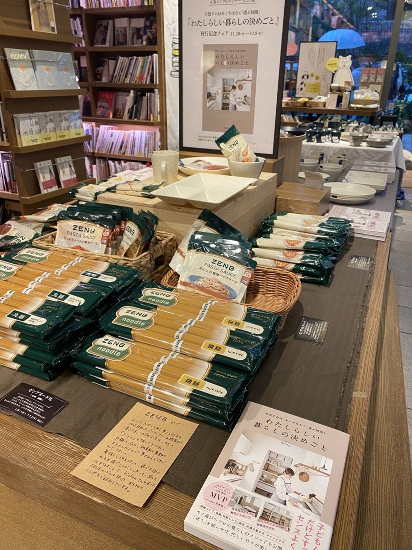 会場の様子。ZENBの麺やパスタソース、器が並び、奥に刊行記念フェアのポスター。
